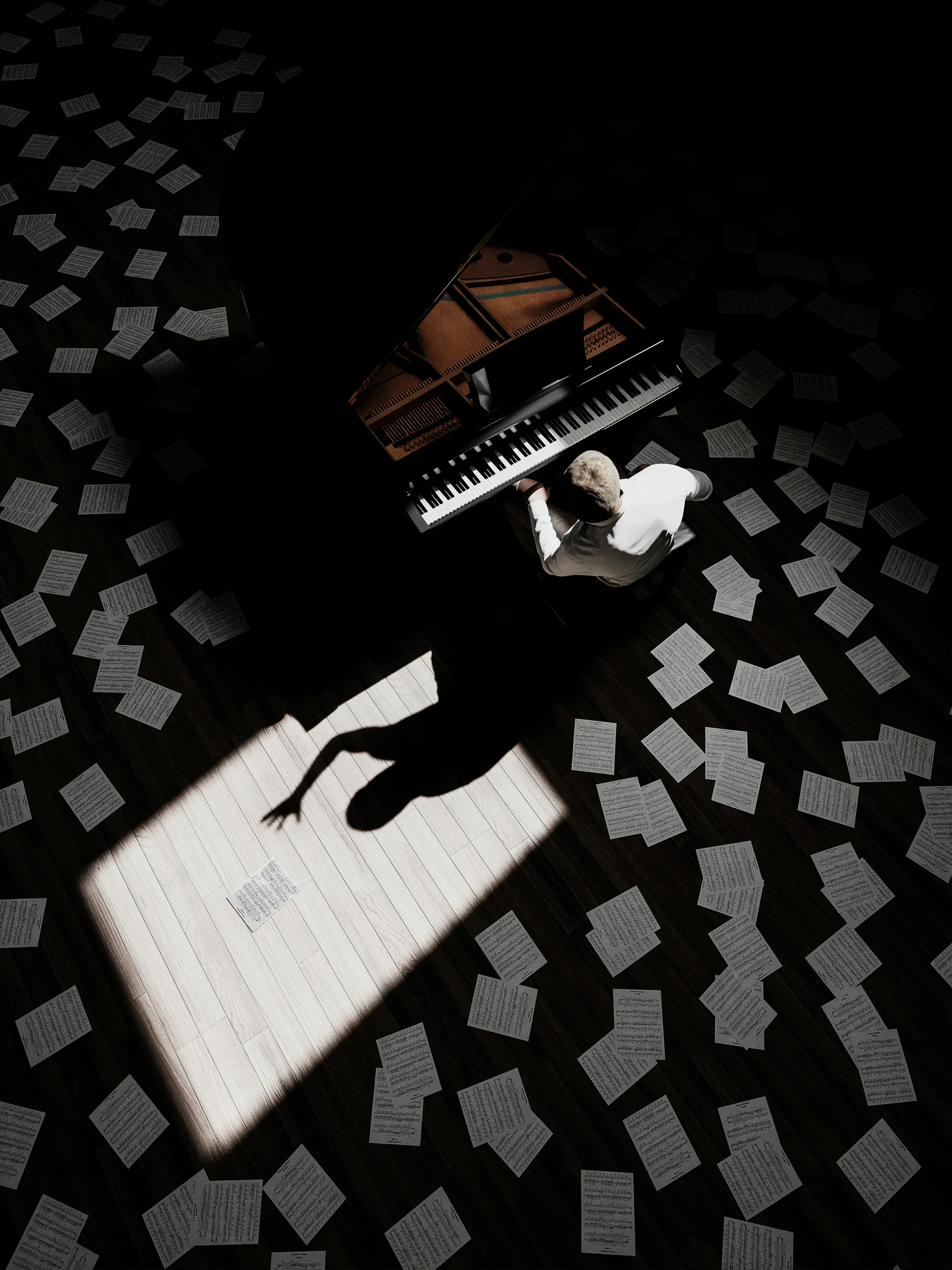 Hombre sentado al piano rodeado de partituras.